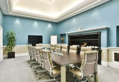 Spacious boardroom with blue walls, a large wooden table, and tan leather chairs.
