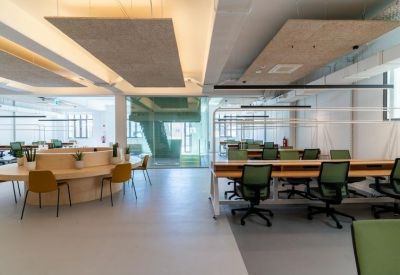 Modern office workspace featuring wooden desks, green chairs, and acoustic ceiling panels.