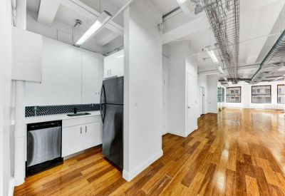 Bright communal kitchen with white cabinetry, stainless dishwasher, and warm wood flooring.