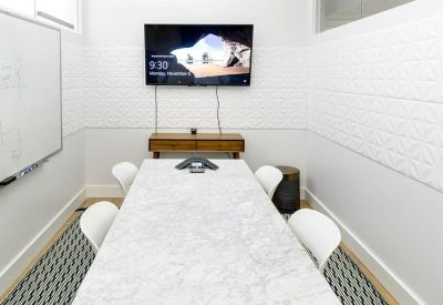 Compact meeting room featuring a marble-topped table, white chairs, and a wall-mounted TV.