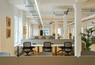 Spacious open-plan office with white pillars, rows of desks, and parquet flooring.