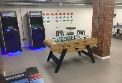 Basement games room with arcade machines, foosball table, and exposed brick.