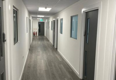 Long, brightly lit office corridor with grey wood-effect flooring.