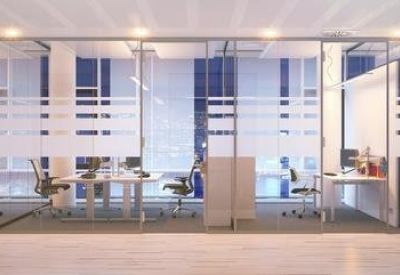 Modern glass-partitioned office workspace with rows of desks under soft recessed lighting.