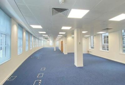 Spacious open-plan office with blue carpeting and rows of bright overhead lighting.
