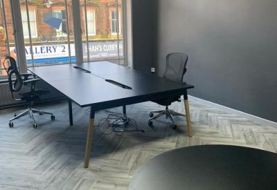 Bright private office featuring a large black desk, herringbone flooring, and large windows.