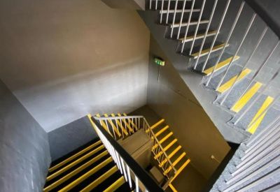 Internal staircase with grey steps, white railings, and high-visibility yellow safety strips.