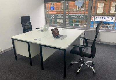 Modern workspace with a two-person white desk, black mesh chairs, and large window with street views.