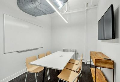 Minimalist meeting room with a white conference table, light wood chairs, and a large wall-mounted screen.