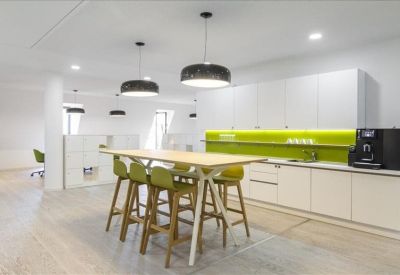 Contemporary office kitchen and breakout space with a high wooden table and lime green backsplash.