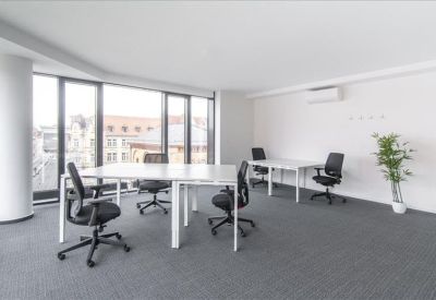 Spacious open-plan office with white desks and large windows overlooking the city.