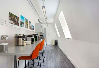 Narrow communal kitchen area with grey counters and bright orange bar stools.
