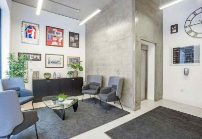 Contemporary reception lounge with grey armchairs, a glass coffee table, and a concrete feature wall.