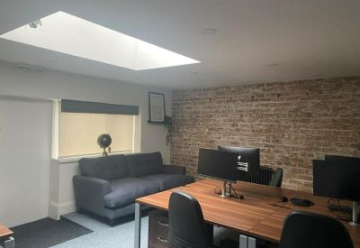 Bright office workspace with wooden desks, a dark sofa, and a large skylight providing natural light.