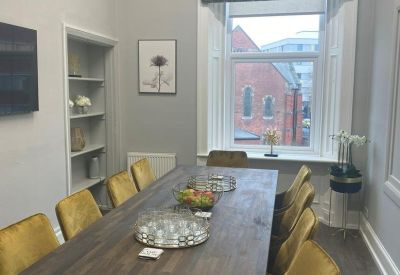 Formal boardroom featuring a long wooden table, mustard yellow velvet chairs, and a patterned window blind.