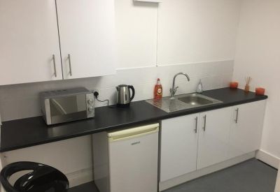 Modern communal kitchen with white cabinetry, black countertops, and a microwave.