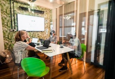 Bright glass-walled meeting room with tropical leaf wallpaper and green chairs.