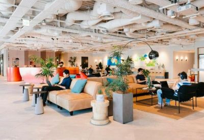 Vibrant open-plan coworking space with tan leather chairs, plants, and an industrial ceiling.