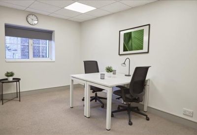 Two-person private office with white desks, black chairs, and a green botanical wall print.