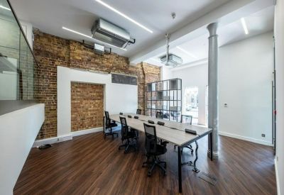Modern office interior with dark wood flooring, brick details, and a central white workstation.