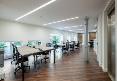 Open-plan workspace with multiple wooden desks, black office chairs, and recessed linear lighting.