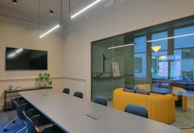 Professional meeting room with a long grey table and view into a yellow lounge area.