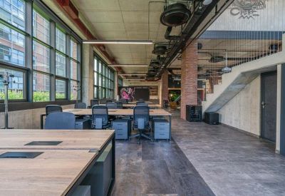 Spacious open-plan office with wooden desks and industrial-style exposed ceilings.