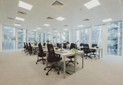 Open-plan office with white desks and black ergonomic chairs.