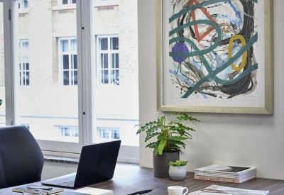 Private office workstation with a wooden desk, laptop, and colorful abstract wall art.