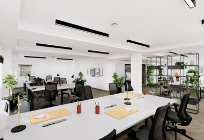 Bright open-plan office space featuring long white desks, ergonomic chairs, and indoor plants.
