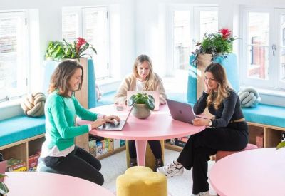 Coworking space with women working at a round pink table near bright windows.