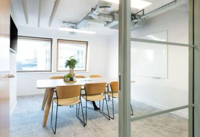 Glass-walled meeting room with a wooden table and comfortable modern chairs.