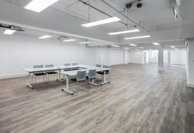 Bright, open-plan meeting area with white tables arranged in a U-shape and wood-effect flooring.