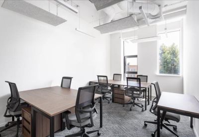 Bright private office with multiple wooden desks and black mesh chairs.
