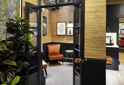 View through dark framed glass doors into a warm breakout room with tan textured wallpaper.