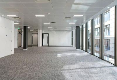 Spacious open-plan office floor with gray carpeting and rows of overhead lighting.