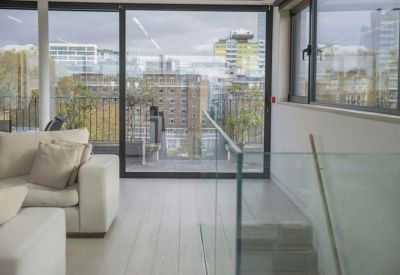 Lounge area with light sofas overlooking a balcony and urban skyline through floor-to-ceiling windows.