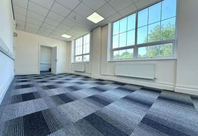 Spacious open-plan office with blue patterned carpet tiles and large windows.