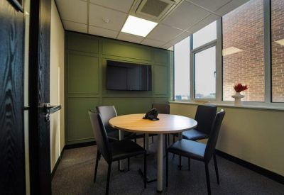 Small meeting room with a round table, teal wall, and large window.