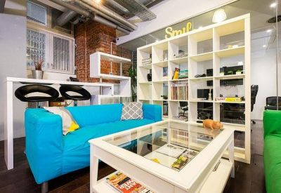 Bright communal lounge with a vibrant blue sofa, white shelving unit, and glass coffee table.