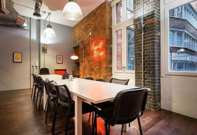Spacious meeting room featuring a long white table, black chairs, and a neon wall sign.