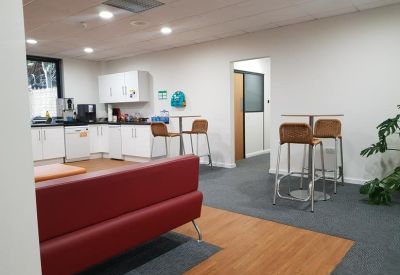Communal kitchen and breakout area featuring a red sofa and wooden breakfast stools.