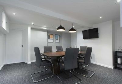 Modern meeting room with a dark wood table, grey chairs, and a wall-mounted TV.