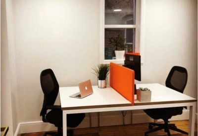 Two-person white desk with orange privacy screen and ergonomic black mesh chairs.
