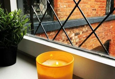 Lit candle on a white windowsill in front of a leaded glass window and brick wall.