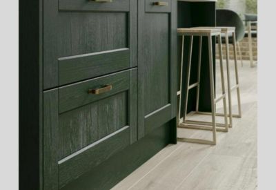 Modern dark green kitchen cabinetry with brass handles and wooden bar stools.