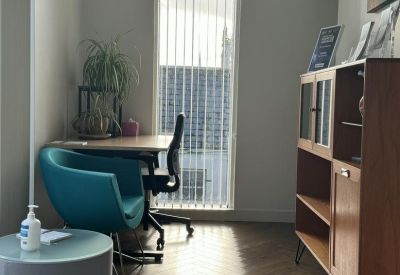 Private office suite with a teal armchair and wooden shelving unit.