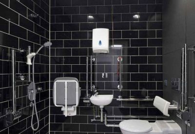 Accessible wet room with black tiled walls, a fold-down shower seat, and white porcelain fixtures.