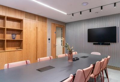 Professional meeting room with a dark grey table, pink chairs, and a large wall-mounted screen.