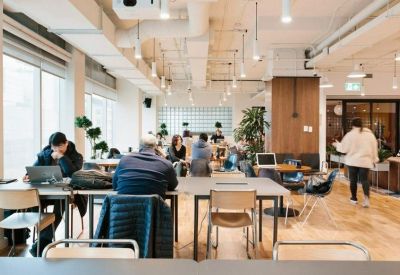 Bright coworking workspace with long shared desks and a warm wood floor.